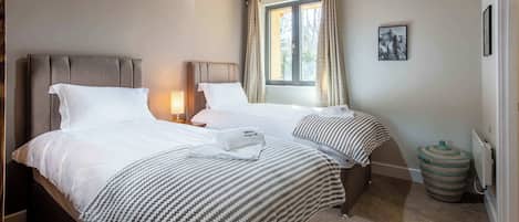 Habitación de hotel con dos camas, una ventana con cortinas, una lámpara, un cuadro en la pared y un radiador.