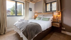 Une chambre à coucher avec un grand lit, une tête de lit en bois, des lampes de chevet et une vue sur les montagnes par les fenêtres.