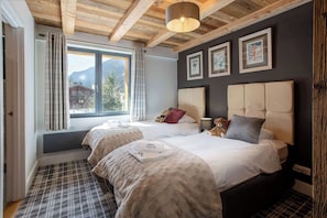 A hotel room with two beds, a large window with a view of mountains, and a ceiling with exposed wooden beams.