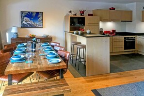 A modern kitchen with wooden cabinets, a central island, and a dining area with a wooden table set for six.