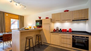 Een moderne keuken met houten kastjes, een inbouwoven en een bar met krukjes.