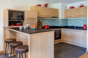 A modern kitchen with wooden cabinets, a black countertop, and a tiled backsplash. - Coin des Drus appt, Golfing, - Chamonix All Year (Les Praz)