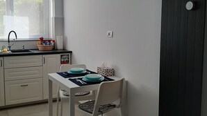 Ett litet kök med vita skåp, ett fönster och ett bord dukat för två personer, med blå tallrikar.