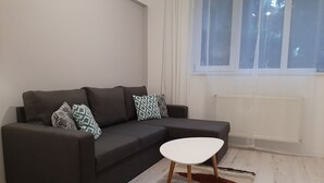 Ett modernt vardagsrum med en mörkgrå hörnsoffa, ett vitt soffbord och en färgglad matta.