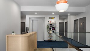 Una moderna zona de recepción con un mostrador de madera, barandilla de cristal y suelo cubierto de moqueta azul.