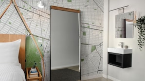 Habitación de hotel moderna con un espejo grande, una cama, una mesita de noche pequeña con una planta y un muro decorado con motivos de mapa.