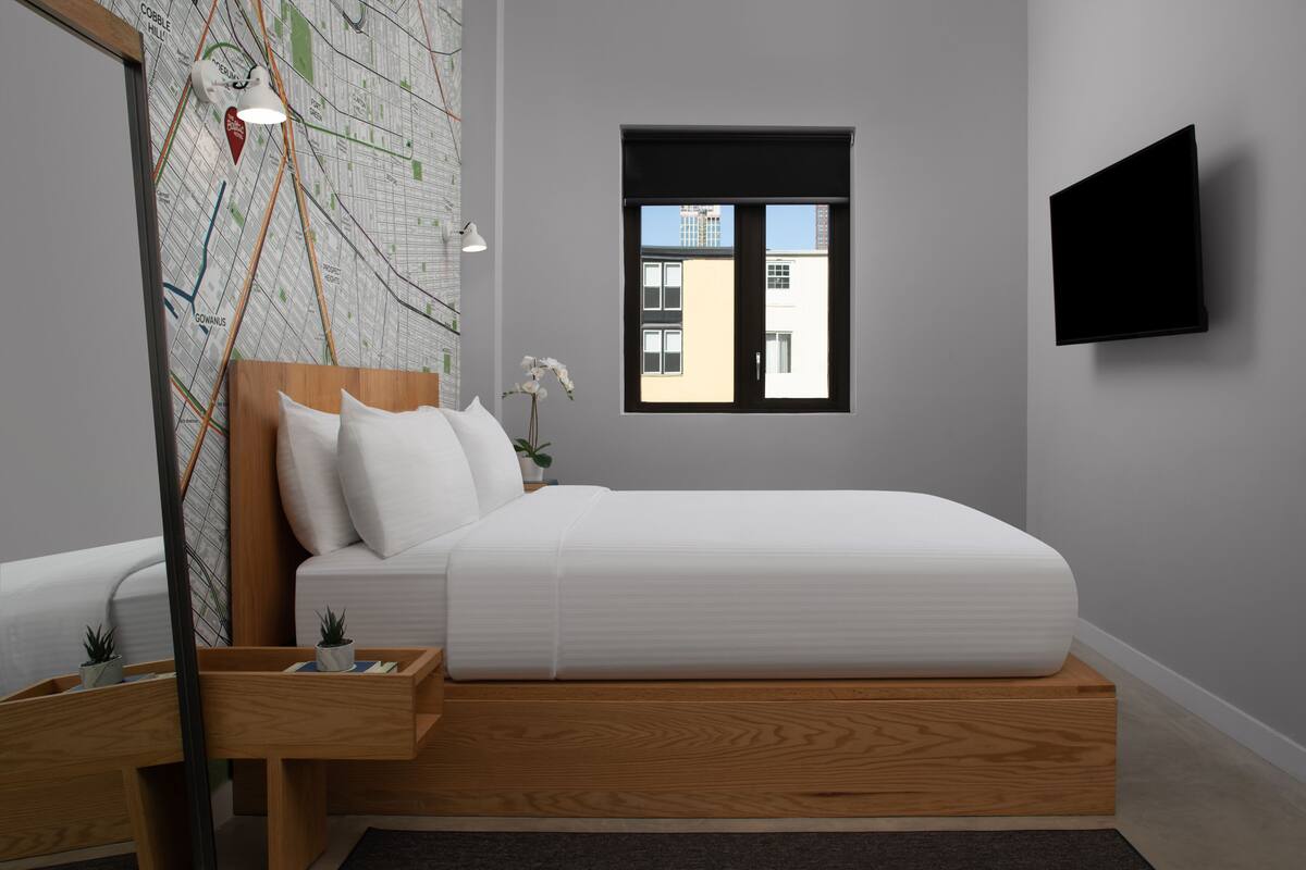 Un dormitorio moderno con una cama de madera, un mural de mapa, una ventana pequeña y un televisor de pantalla plana.