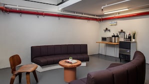 Un espacio de oficina moderno con un sofá marrón oscuro, una mesa redonda de madera y una pequeña silla de madera.