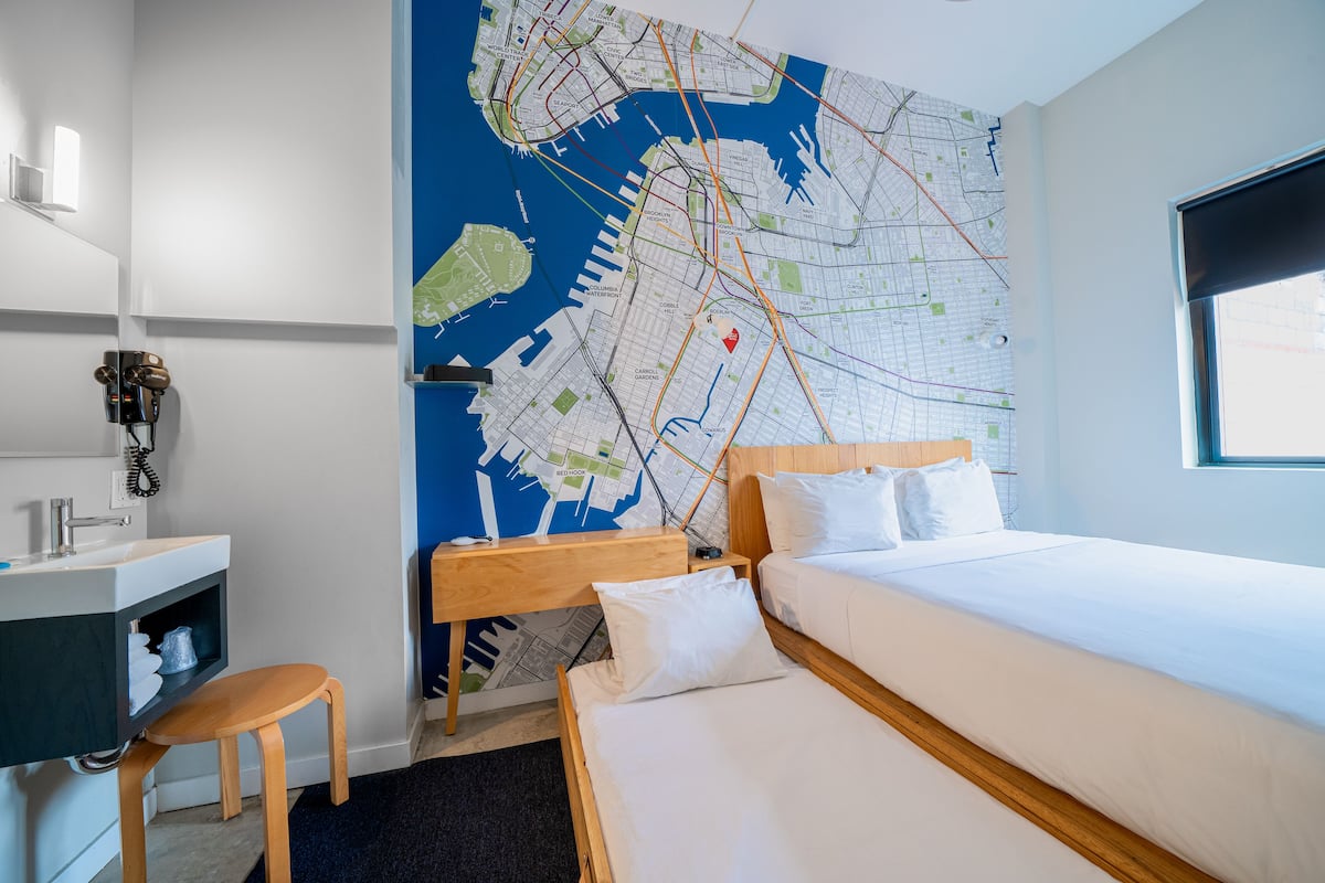 Habitación de hotel con un mapa grande en la pared, una cama, un escritorio con una silla y una ventana.