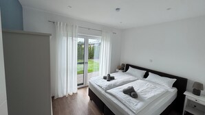 Un dormitorio con cama doble, una mesita de noche, una lámpara y vista a un jardín a través de una puerta corrediza de vidrio.