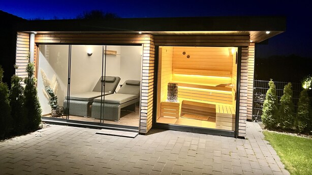 Una sauna moderna y bien iluminada con paredes de vidrio, un banco y un interior de madera.