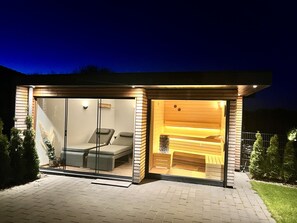 Una sauna moderna y bien iluminada con paredes de vidrio, un banco y un interior de madera.