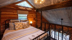 Een gezellig houten slaapkamer met een bed, kussens, een nachtkastje en een raam.