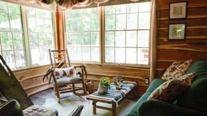 Een knus interieur van een chalet, met een schommelstoel, een groene bank en een houten bankje.