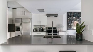 A modern kitchen with stainless steel appliances, a central island, and two black bar stools. - High-Spec Opulent Townhouse in Oak Lawn (Dallas)