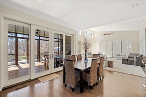 A spacious dining area with a large table and wicker chairs, a modern kitchen in the background, and a view of the outdoors through large sliding glass doors. - Lakefront Escape w/ Boathouse & Helipad – Your Ultimate Lake Gaston Getaway (Littleton)