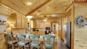 Interior de una cabaña de madera con una isla de cocina, sillas y un refrigerador.