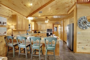 A wooden cabin interior with a kitchen island, chairs, and a refrigerator.
