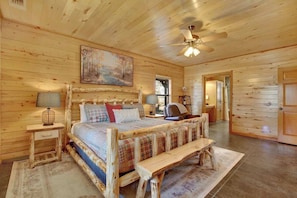 Une chambre dans un chalet en rondins, avec un lit en bois, un ventilateur de plafond, un tableau et un banc.
