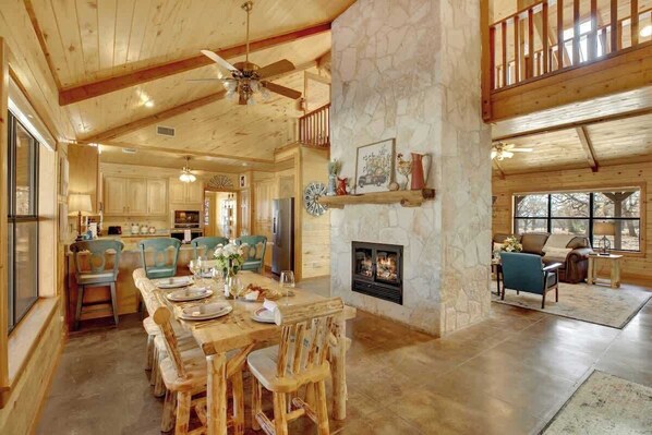 A spacious living area with a stone fireplace, wooden furniture, and a high ceiling with exposed beams.
