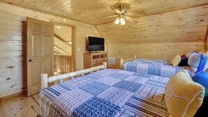 Un dormitorio de cabaña de madera con dos camas, un ventilador de techo, un televisor y una puerta de madera.