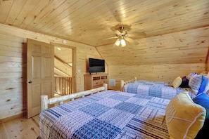 A wooden cabin bedroom with two beds, a ceiling fan, a TV, and a wooden door.