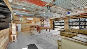 A rustic interior with a wooden wall, a pool table, a sofa, and a bar area.