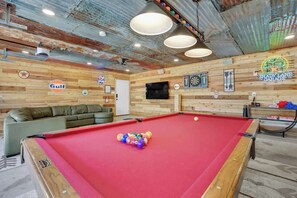 Ein Billardtisch mit Kugeln, ein grünes Sofa und eine Dartscheibe in einem Raum mit Holzwänden und -decke.