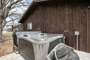 Un bain à remous à l’extérieur d’un bâtiment en bois, avec un espace salon couvert à proximité.