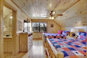 Eine Holzhütte mit Deckenventilator, zwei Betten mit Bettdecken, einem Schminktisch und einem Fenster mit Blick auf Bäume.