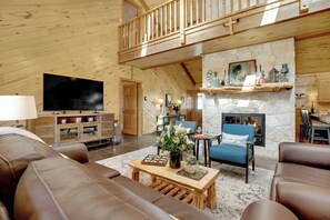 Ein großzügiger Wohnbereich im Loft-Stil mit Kamin, Ledersofas, einem Flachbildfernseher und einer Holzbalkendecke.