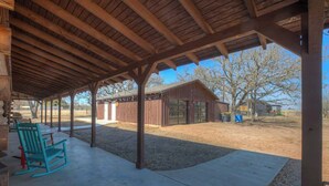 A covered outdoor area with a concrete floor, wooden beams, and a view of a building with windows and a door.