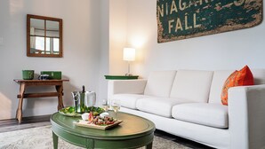 A living room with a white sofa, a green coffee table, a wooden side table with a camera, a pitcher, and glasses. - Kent Motel Niagara on the Lake (Niagara-on-the-Lake)