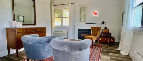 A room with a fireplace, two armchairs, a patterned rug, a wooden cabinet, and a large mirror.