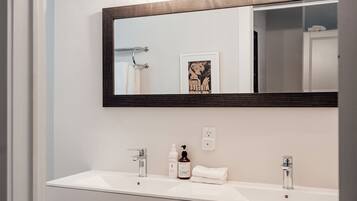 A bathroom with a white vanity, two sinks, a mirror, and a towel rack.