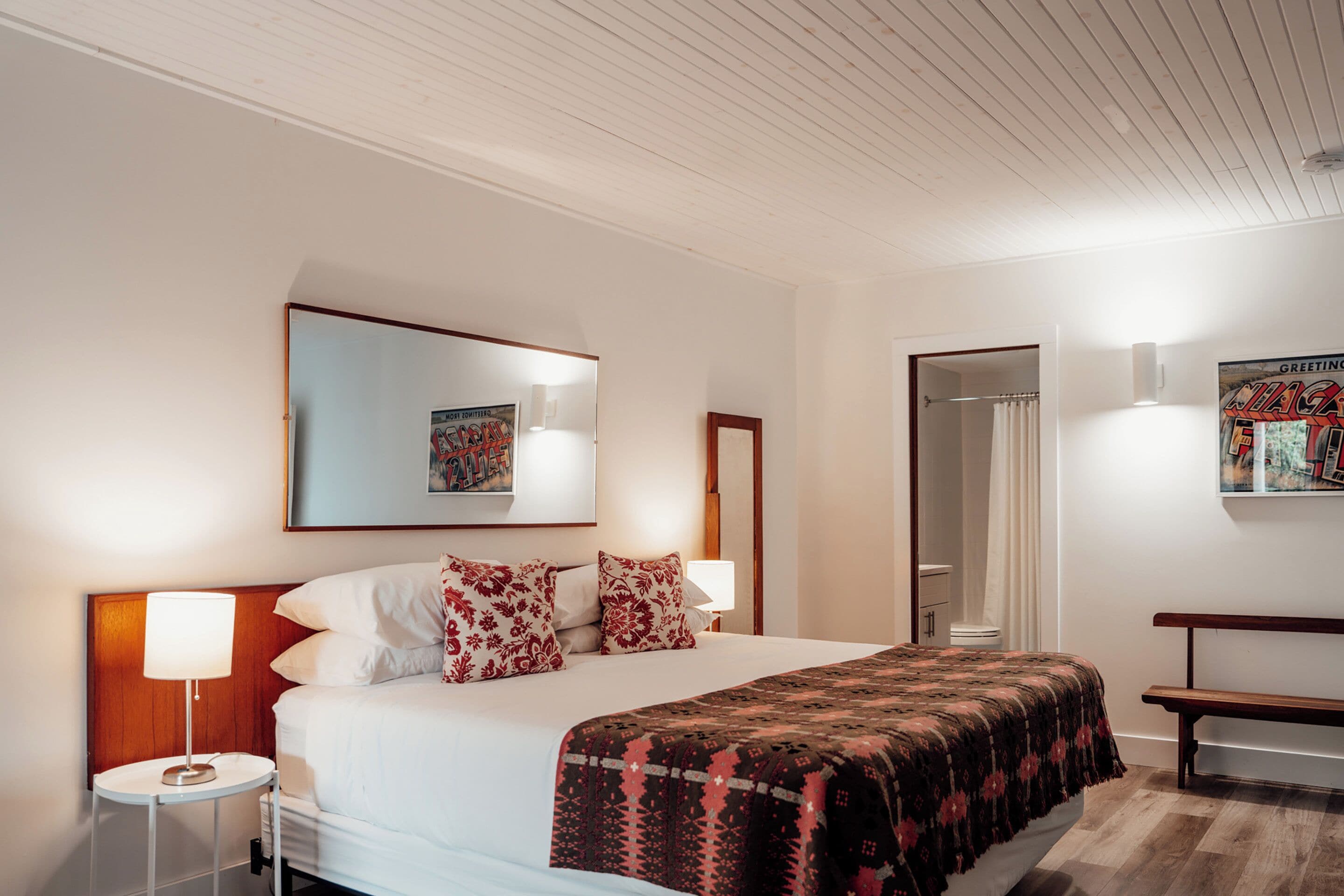 A hotel room with a bed, bedside lamps, a bench, a mirror, and a framed picture on the wall.