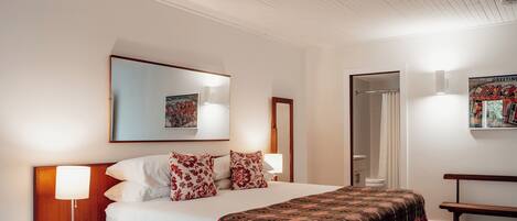 A hotel room with a bed, bedside lamps, a bench, a mirror, and a framed picture on the wall.