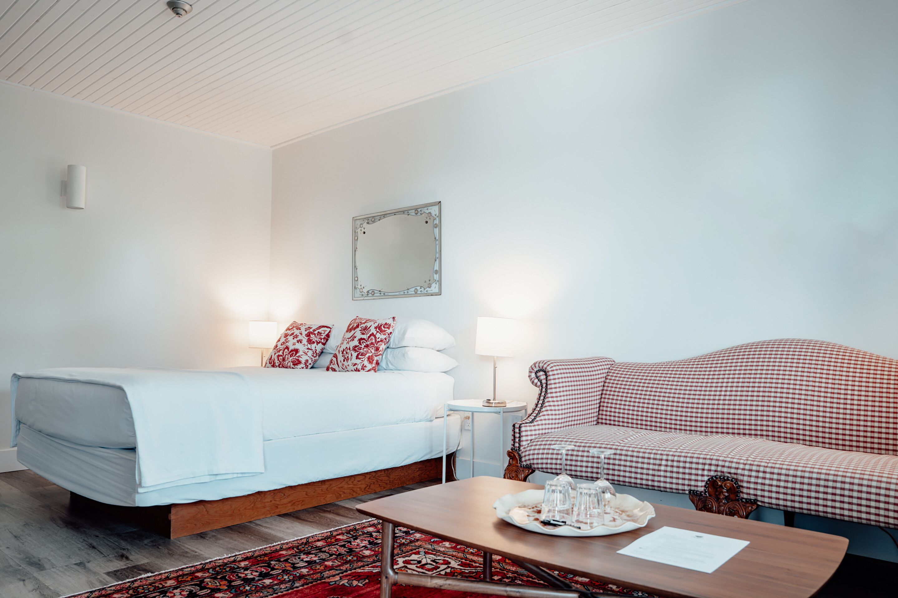 A bedroom with a bed, a bedside table with a lamp, a checkered sofa, and a coffee table with a tray.