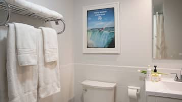 A bathroom with white tiles, a toilet, a sink with toiletries, and two towels hanging on a rack.