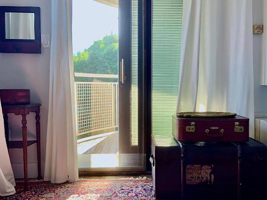 A room with a large sliding glass door leading to a balcony, a patterned carpet, a wooden table, and a suitcase.