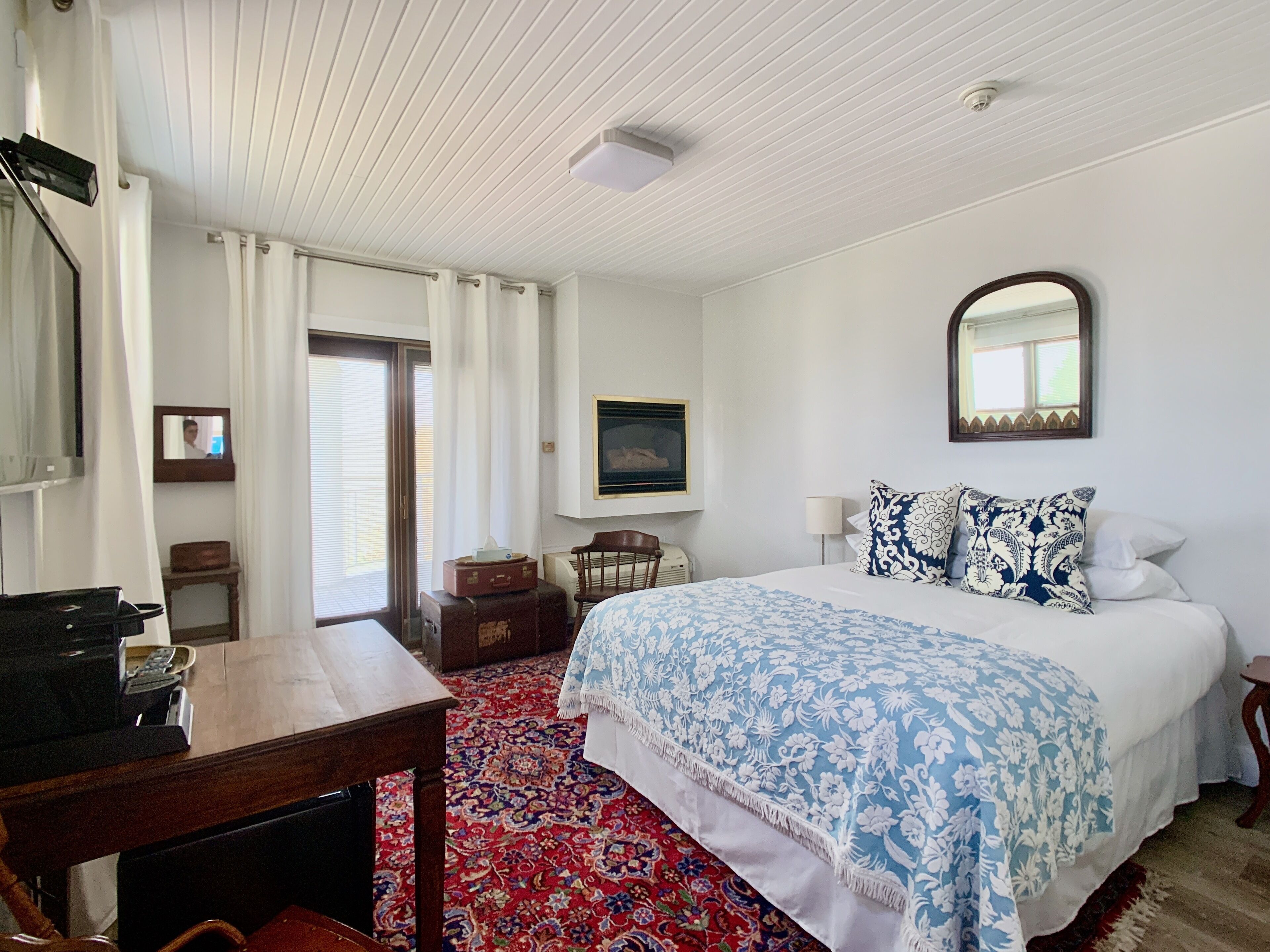 Habitación de hotel con cama, escritorio, silla, espejo y ventana con cortinas.