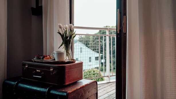 A room with a window, a wooden table, a vase with flowers, a cup, and a plate with pastries. - Kent Motel Niagara on the Lake (Niagara-on-the-Lake)