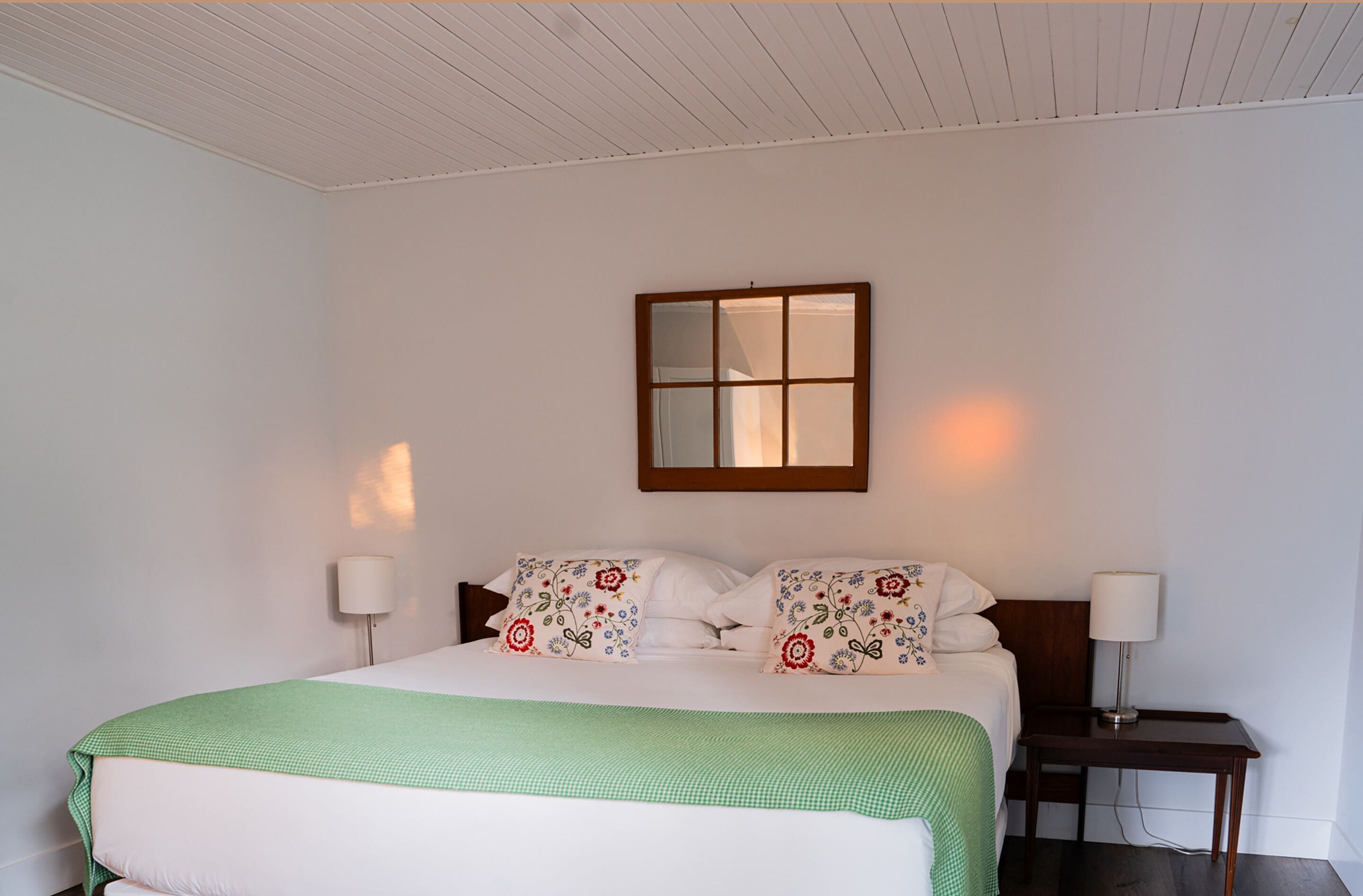 A bedroom with a bed, two bedside lamps, a nightstand, and a window with a wooden frame.