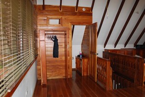 Un interior de madera con techo alto, un banco y una puerta que da a otra habitación.