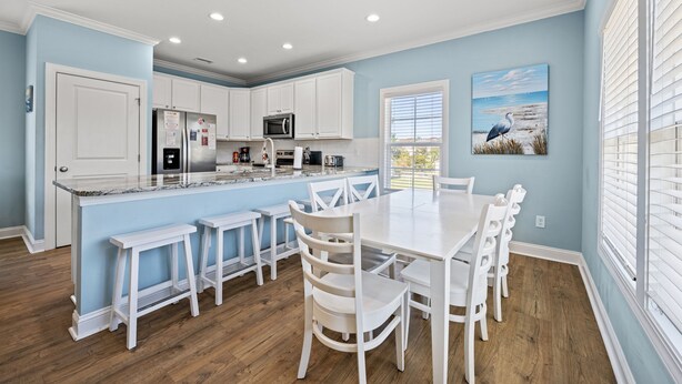 A modern kitchen with white cabinetry, a granite countertop, and a dining area with white chairs and a table. - 1 Precious Memory - 4 Bed/3 Bath - Private Pool (North Myrtle Beach)