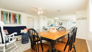 A dining area with a wooden table and chairs, a ceiling fan, and a kitchen in the background. - Pineapple by the Sea - Outdoor Bar, Walk to Beach! (Jamaica Beach)