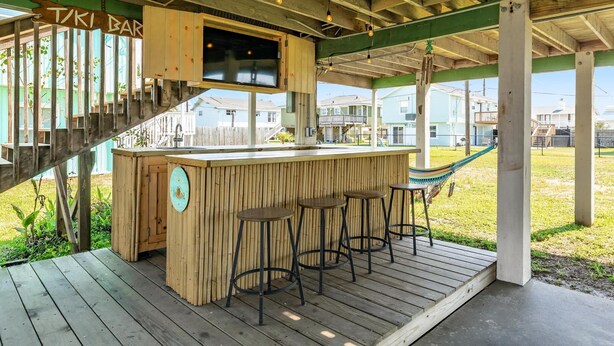 A wooden bar area with a sign reading "TIKI BAR," a wooden counter, and three stools. - Pineapple by the Sea - Outdoor Bar, Walk to Beach! (Jamaica Beach)