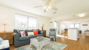 A spacious living area with a grey sofa, a glass coffee table, and a patterned rug. - Pineapple by the Sea - Outdoor Bar, Walk to Beach! (Jamaica Beach)