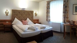 Ein Hotelzimmer mit einem großen Bett, zwei Nachttischen, einem Schreibtisch und einem Fenster mit Vorhängen.
