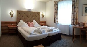 Ein Hotelzimmer mit einem großen Bett, zwei Nachttischen, einem Schreibtisch und einem Fenster mit Vorhängen.